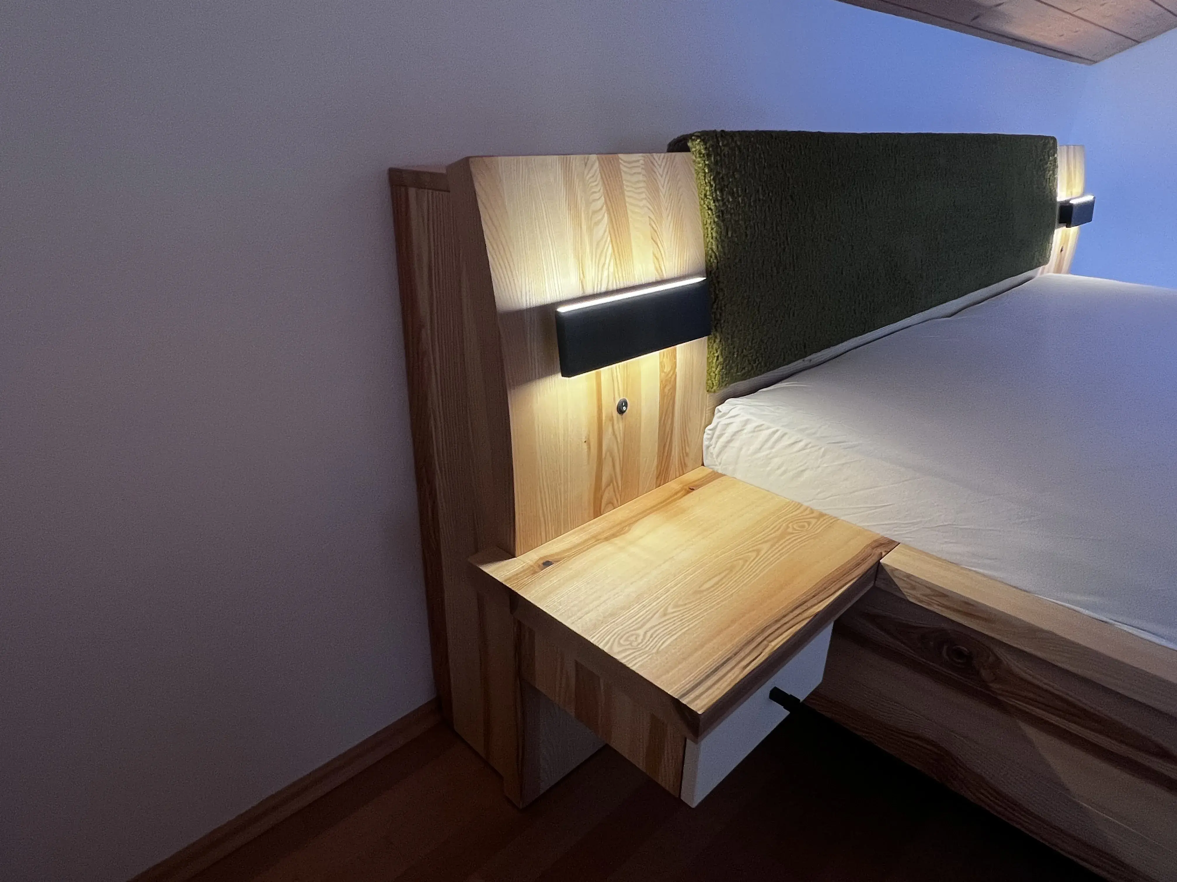 Holzbett mit integriertem Nachttisch und LED-Leuchte an der Wand.