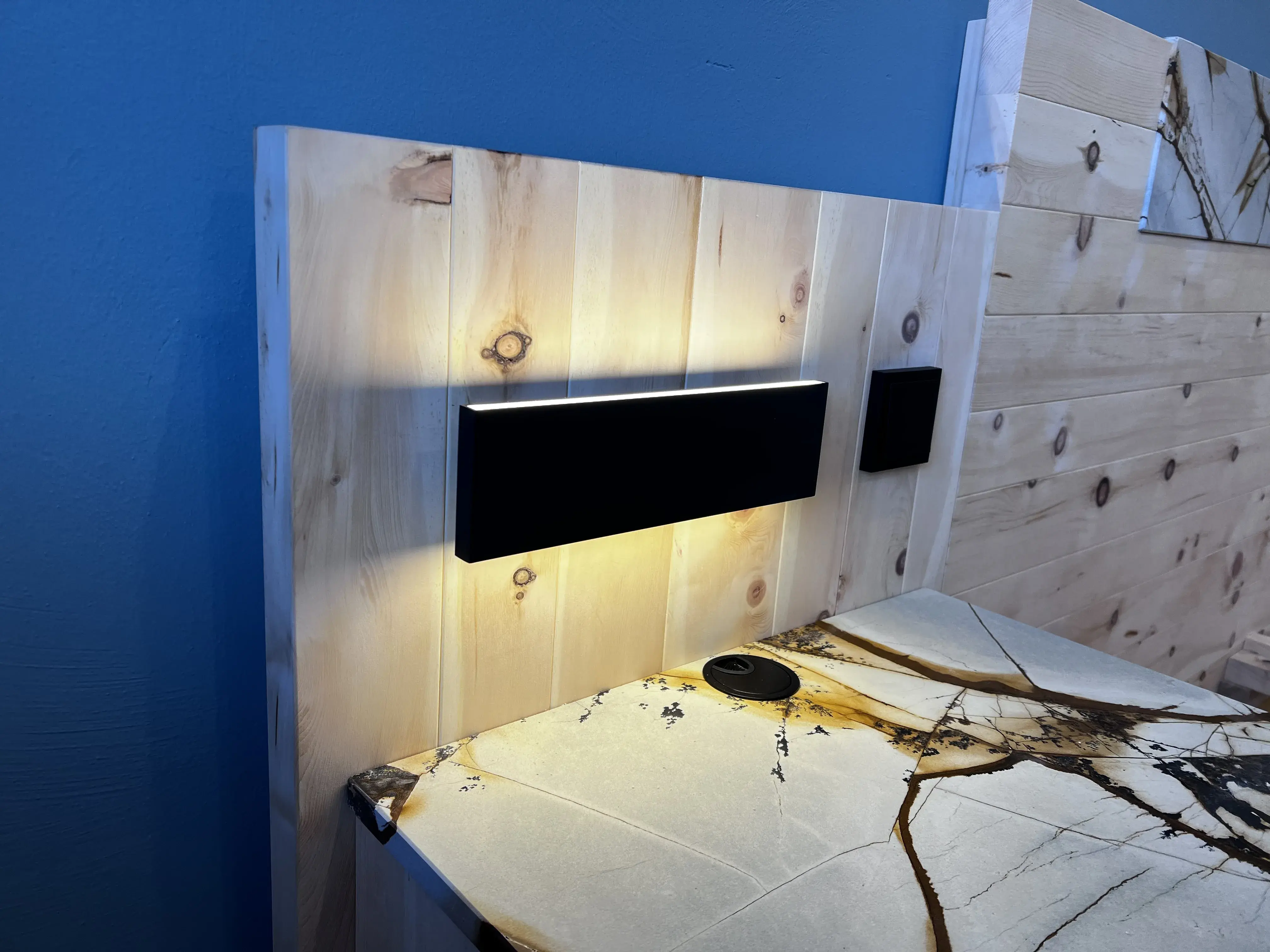 Holzbett mit beleuchtetem Kopfteil und moderner schwarzer Wandlampe.