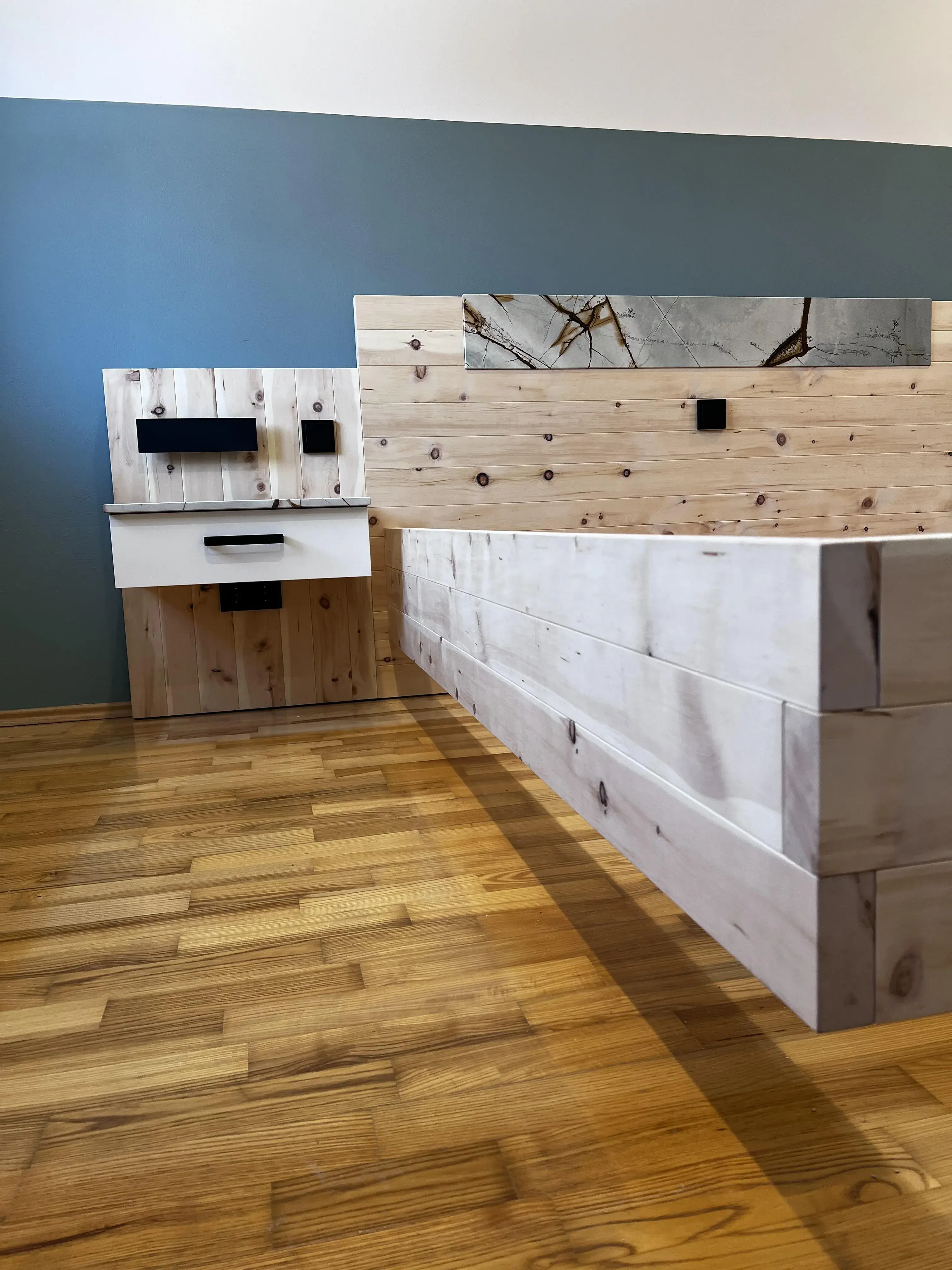 Moderner Empfangstresen aus hellem Holz auf Parkettboden vor blauer Wand.