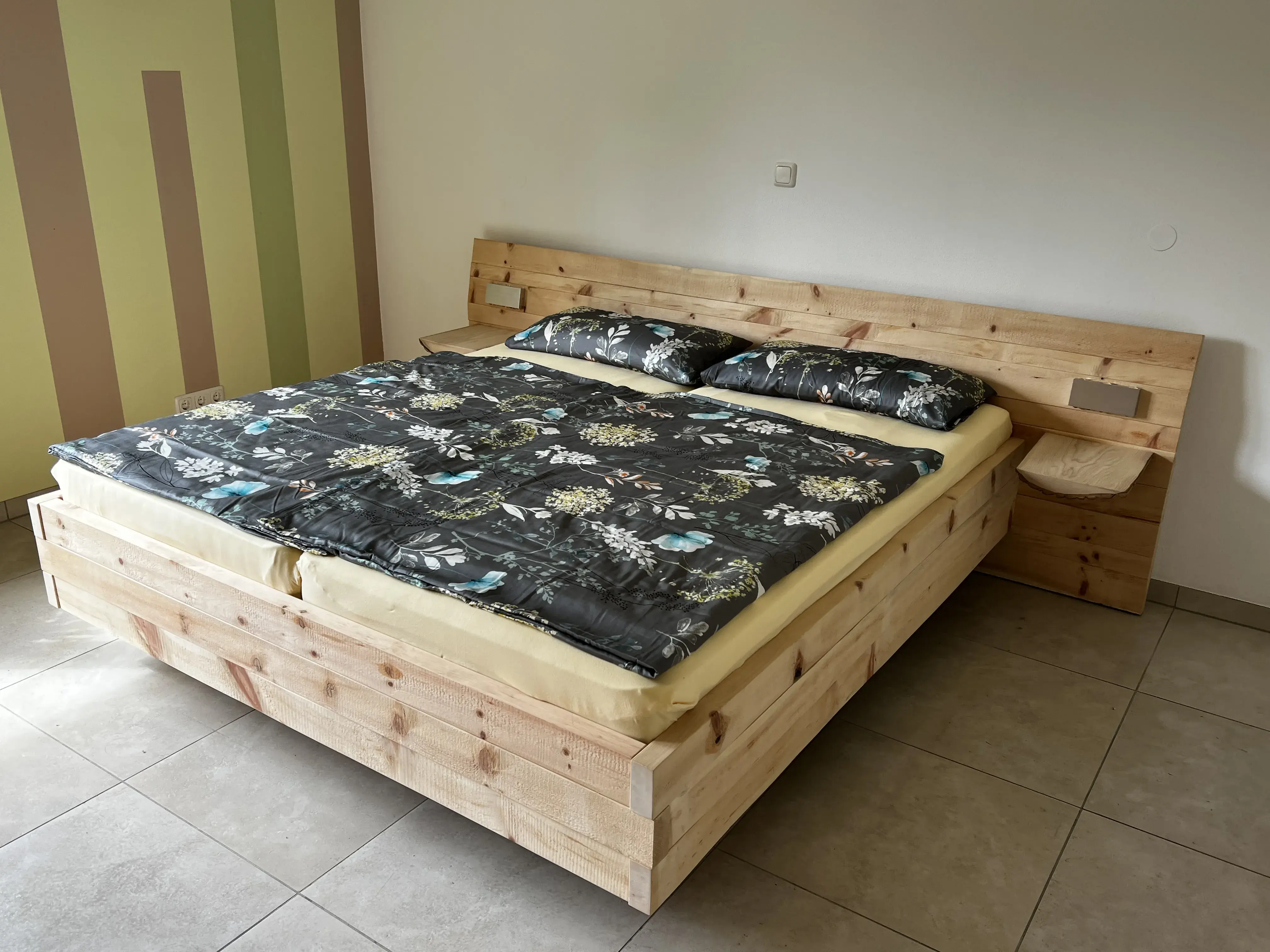 Doppelbett aus hellem Holz mit dunkler Bettwäsche in schlichtem Schlafzimmer.
