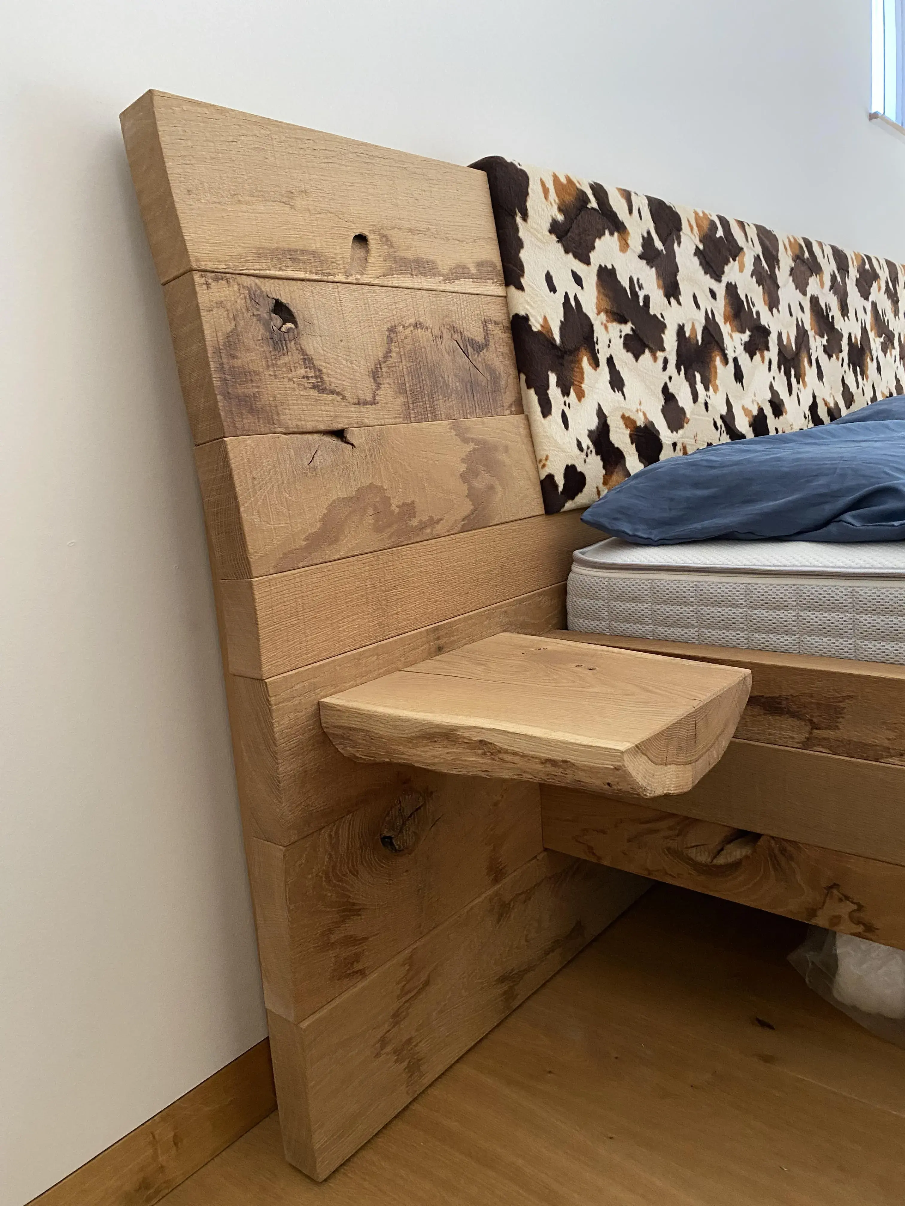 Bett mit massivem Holzkopfteil, integriertem Nachttisch und Kuhfell-Polster.