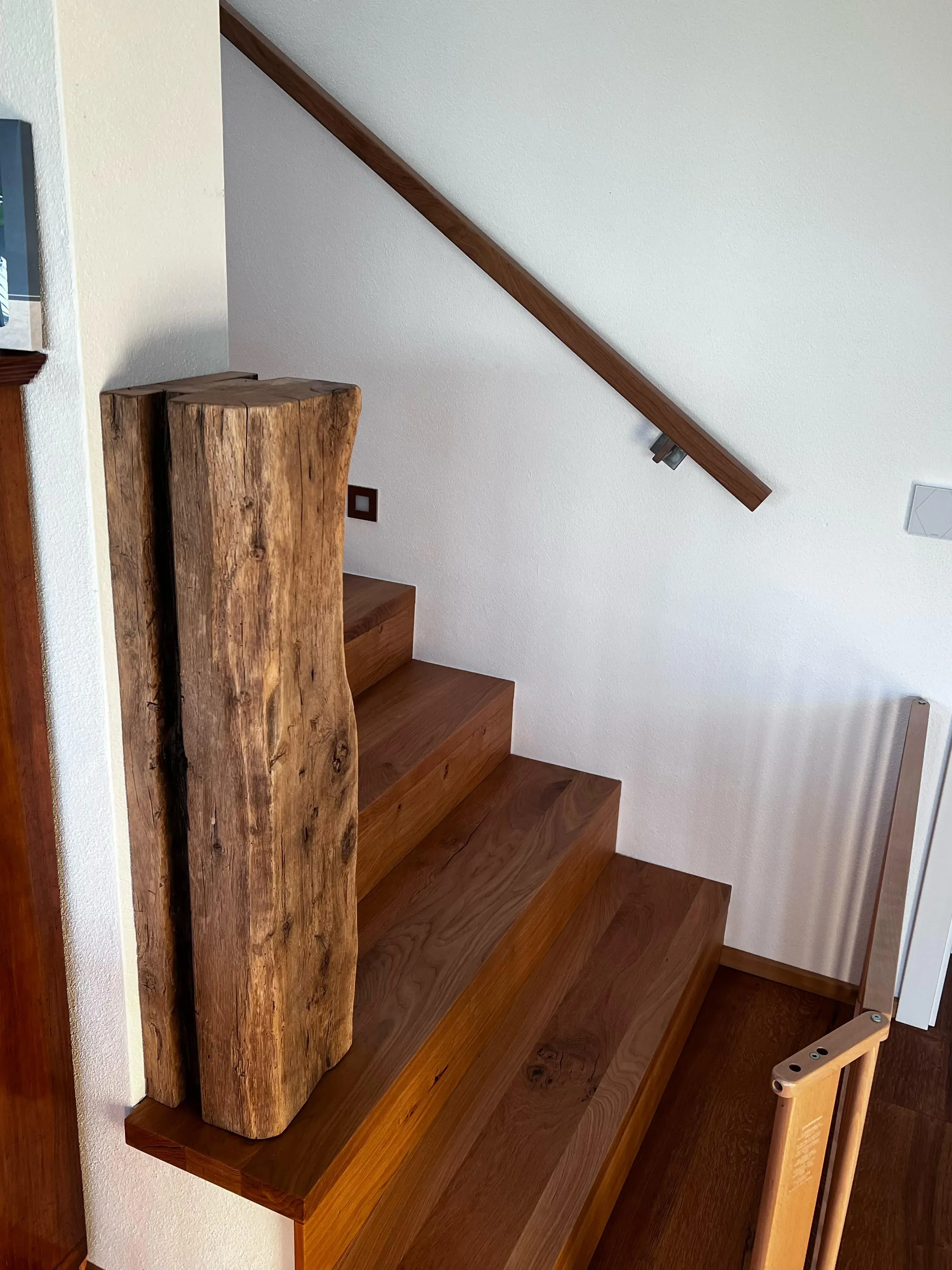 Holztreppe mit dickem, unbearbeitetem Holzpfosten als Geländerstütze.