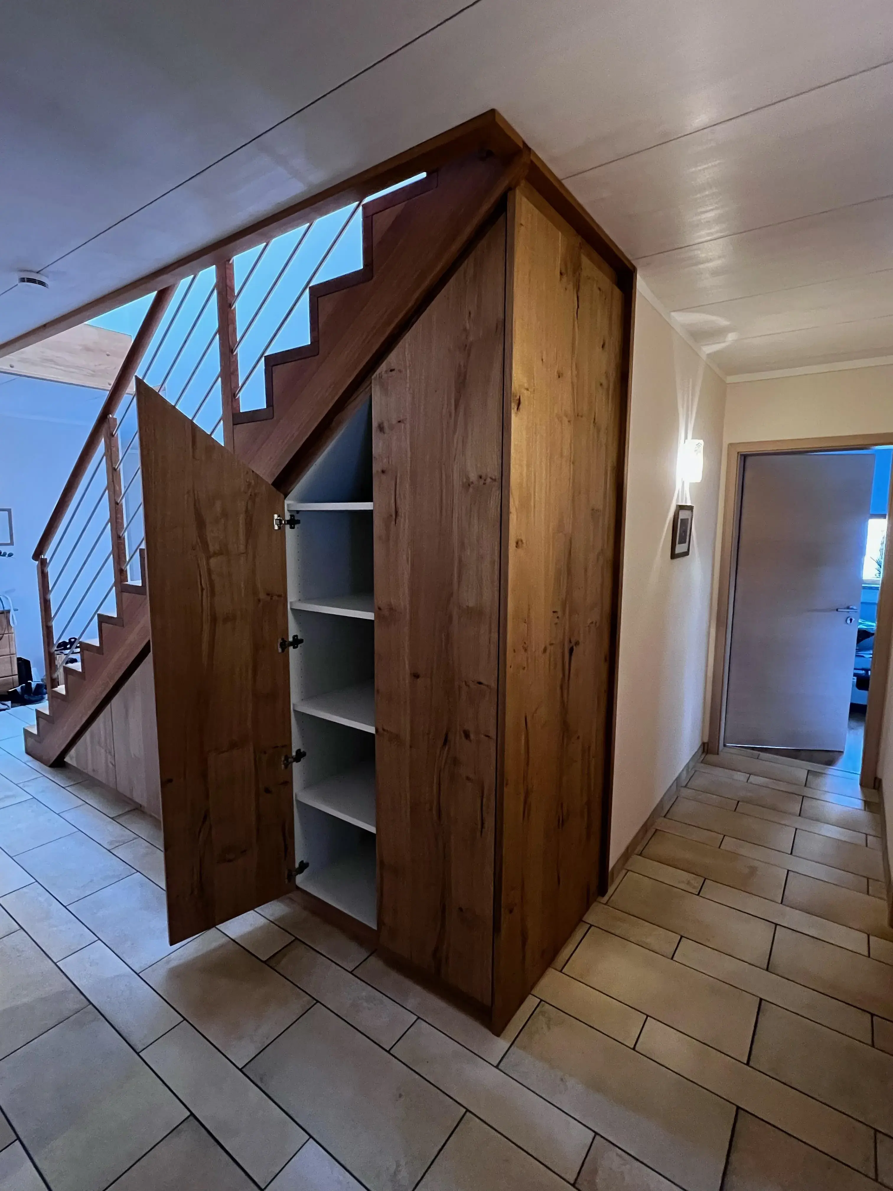 Offener Einbauschrank unter einer Holztreppe mit weißen Regalböden