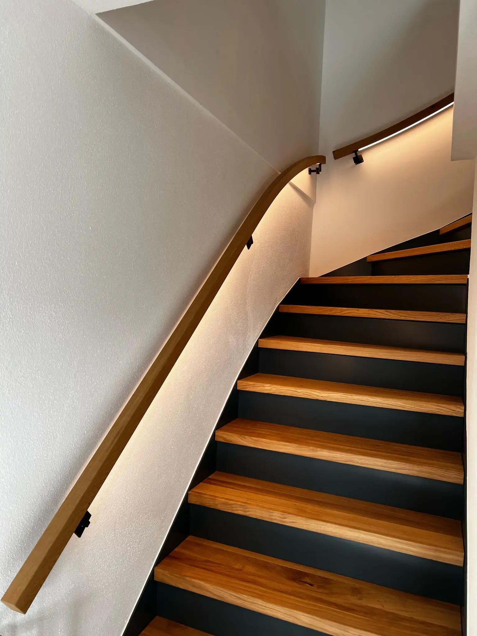 Moderne Holztreppe mit indirekter Beleuchtung und weißer Wand.