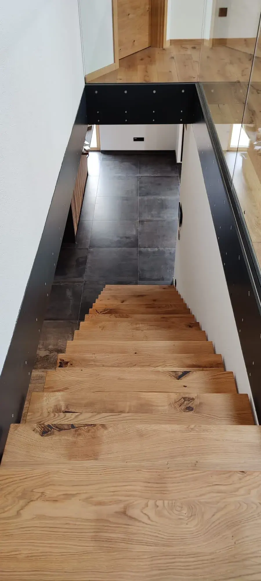 Holztreppe mit schwarzem Geländer führt in einen dunklen Flur hinab.