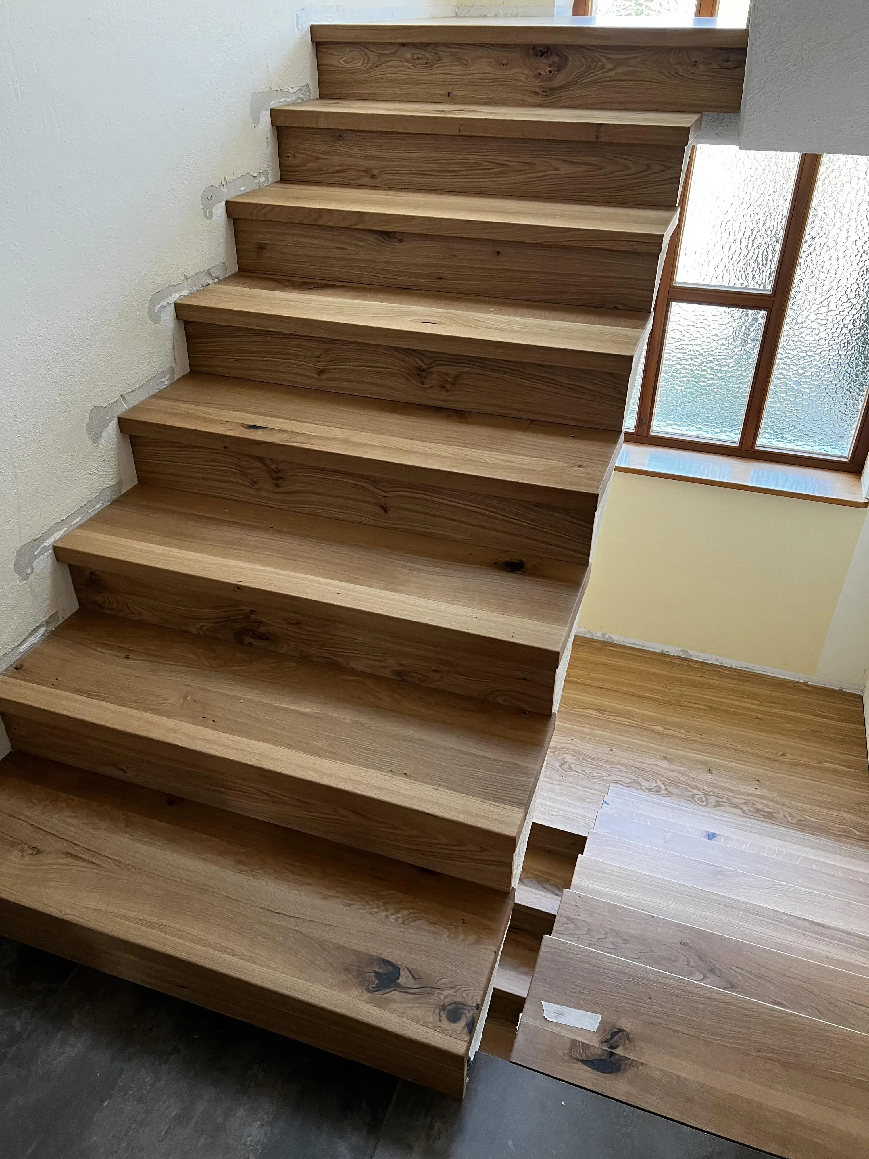 Holztreppe mit breiten Stufen, Fenster im Hintergrund, Tageslicht fällt herein.