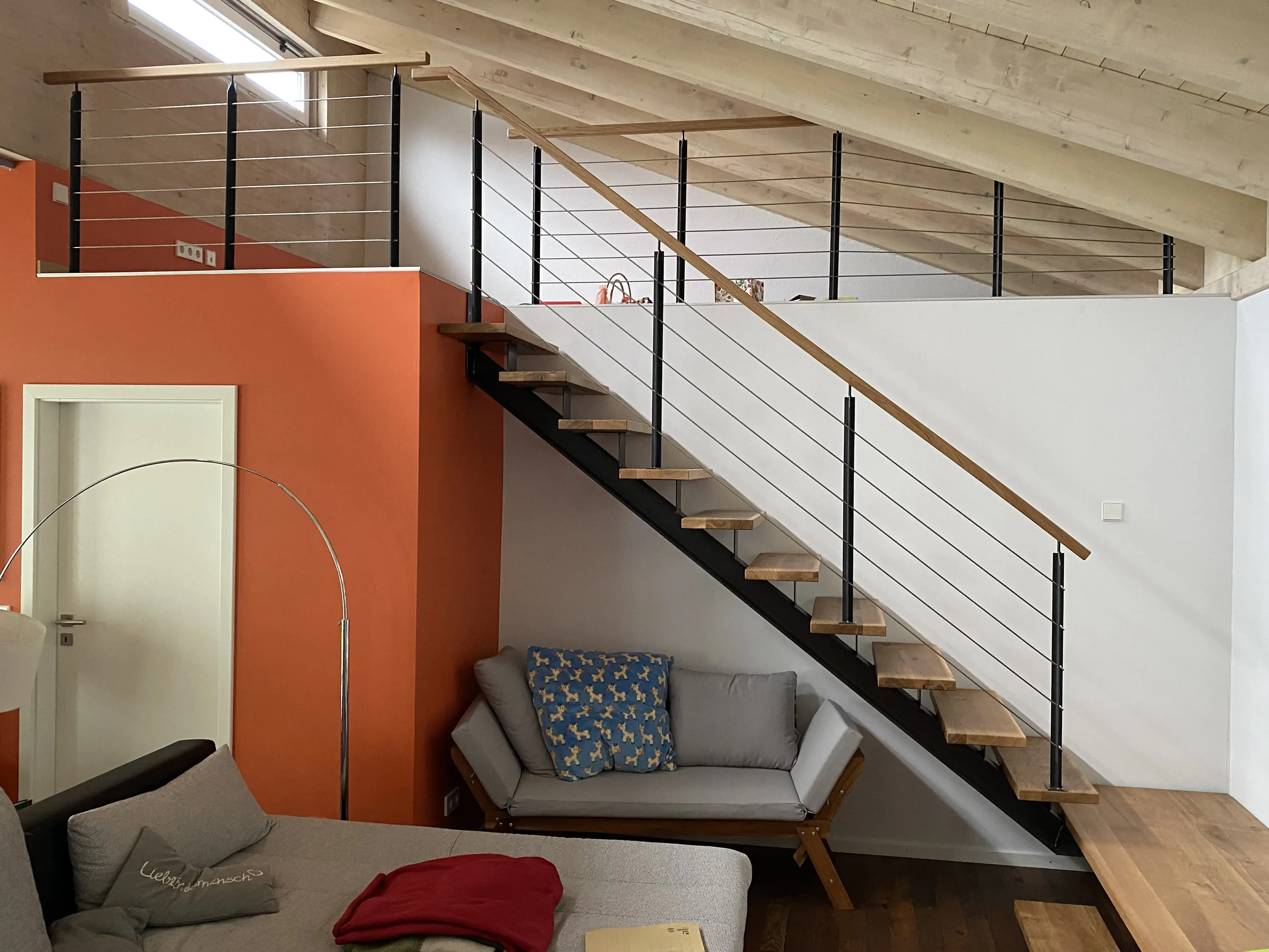 Modernes Wohnzimmer mit Holztreppe, orangefarbener Wand und grauem Sofa.