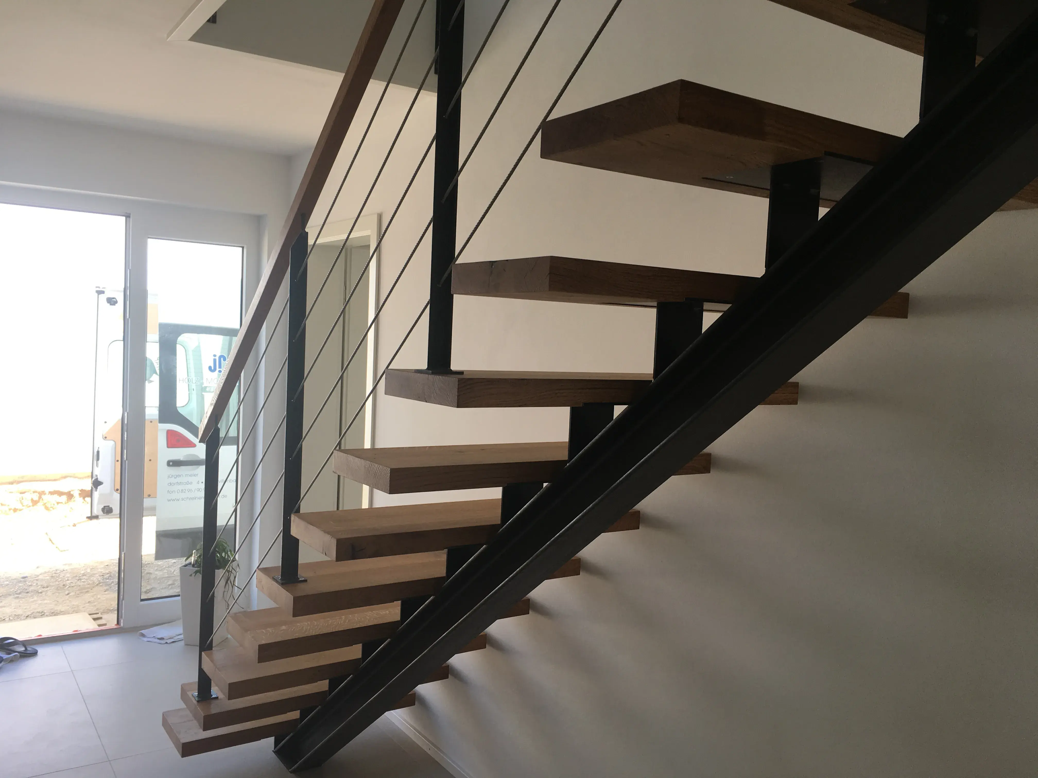 Moderne Holztreppe mit Metallgeländer in hellem, sonnigem Eingangsbereich