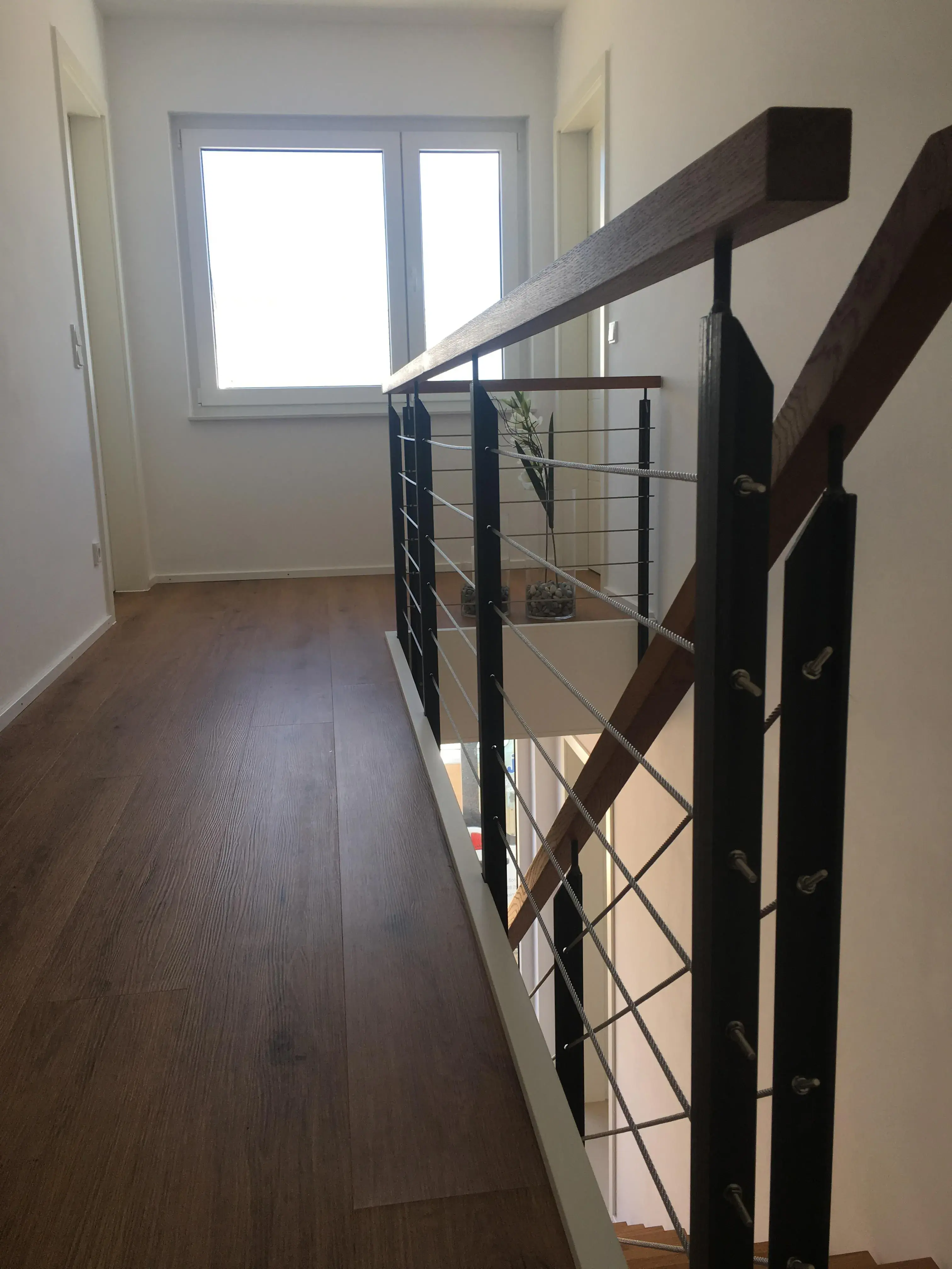 Heller Flur mit Holzfußboden und modernem Geländer, Fenster am Ende.