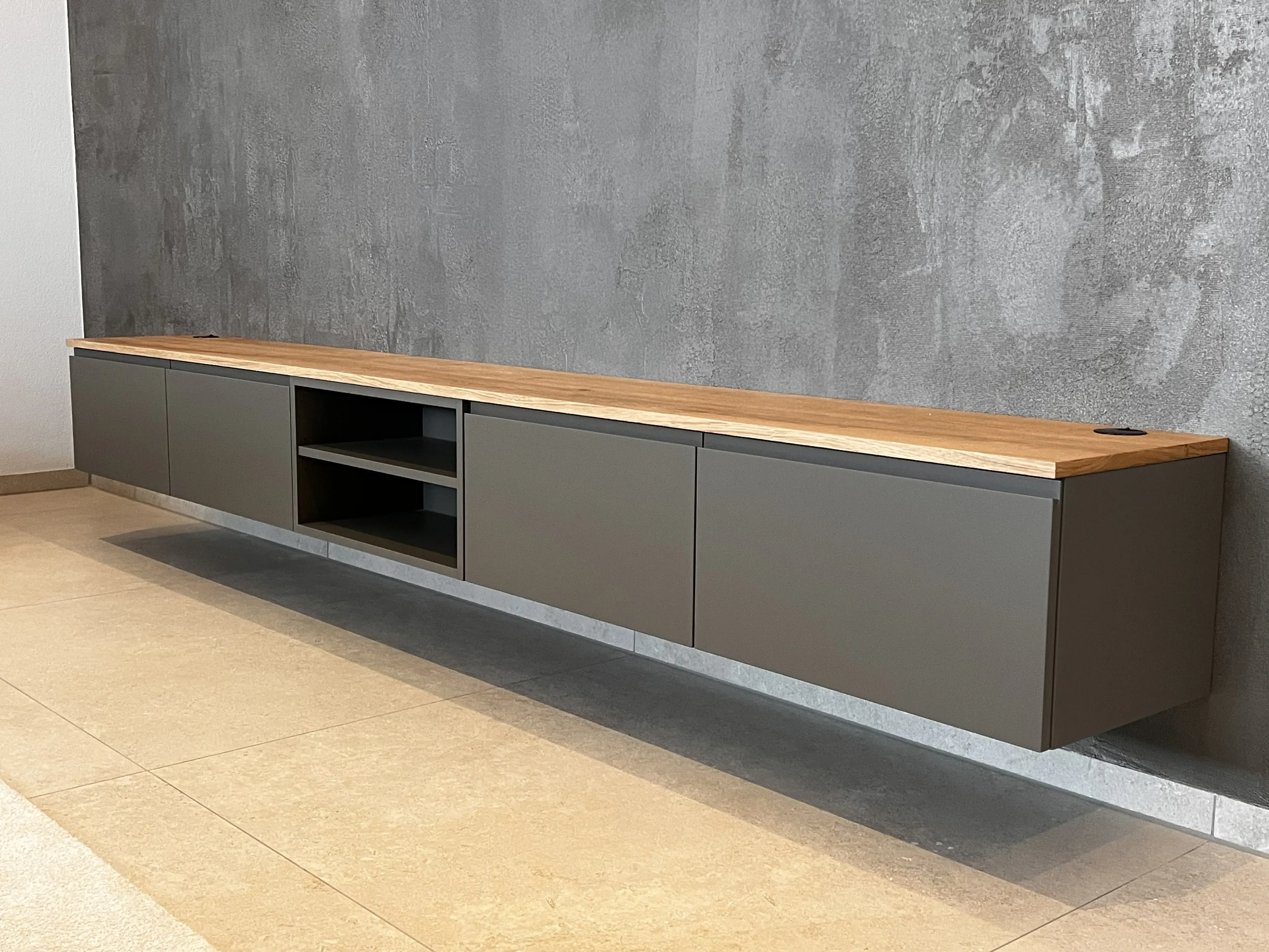 Graues, wandhängendes Sideboard mit Holzplatte vor Betonwand
