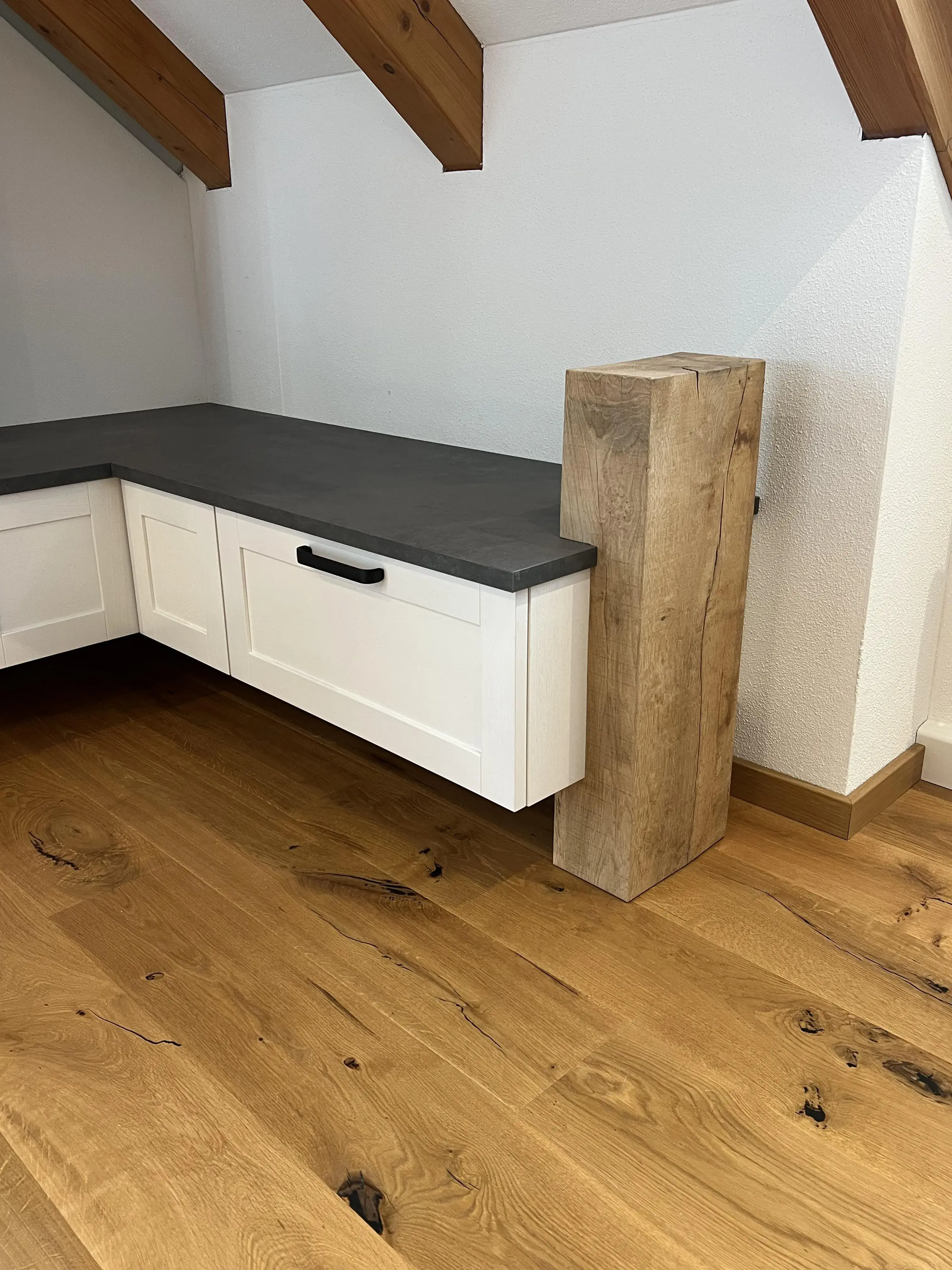 Ecke einer Küche mit weißem Unterschrank, grauer Arbeitsplatte und Holzboden
