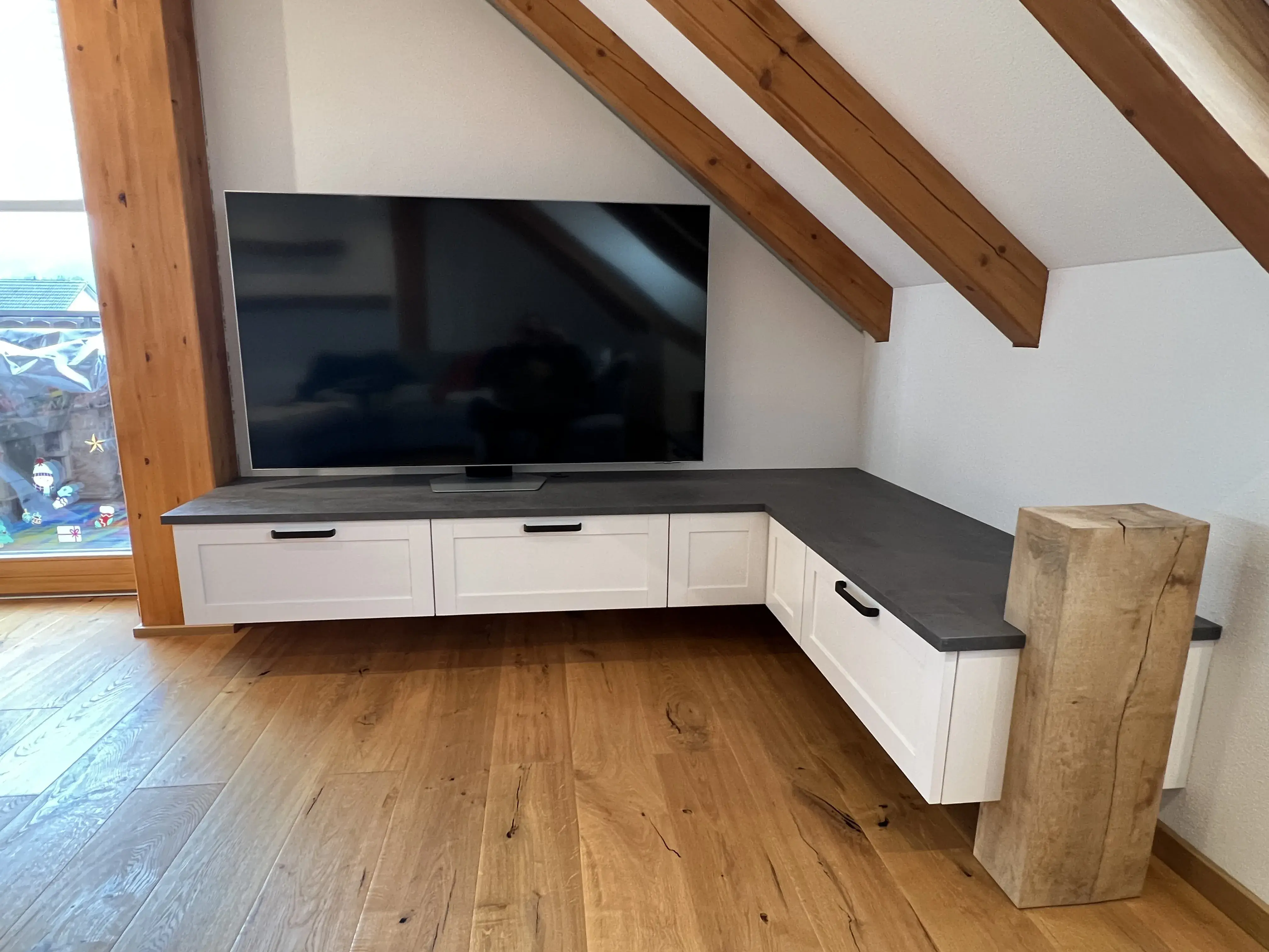 Flachbildfernseher auf weißem Eck-TV-Schrank mit Schubladen, Holzbalken und Parkettboden.