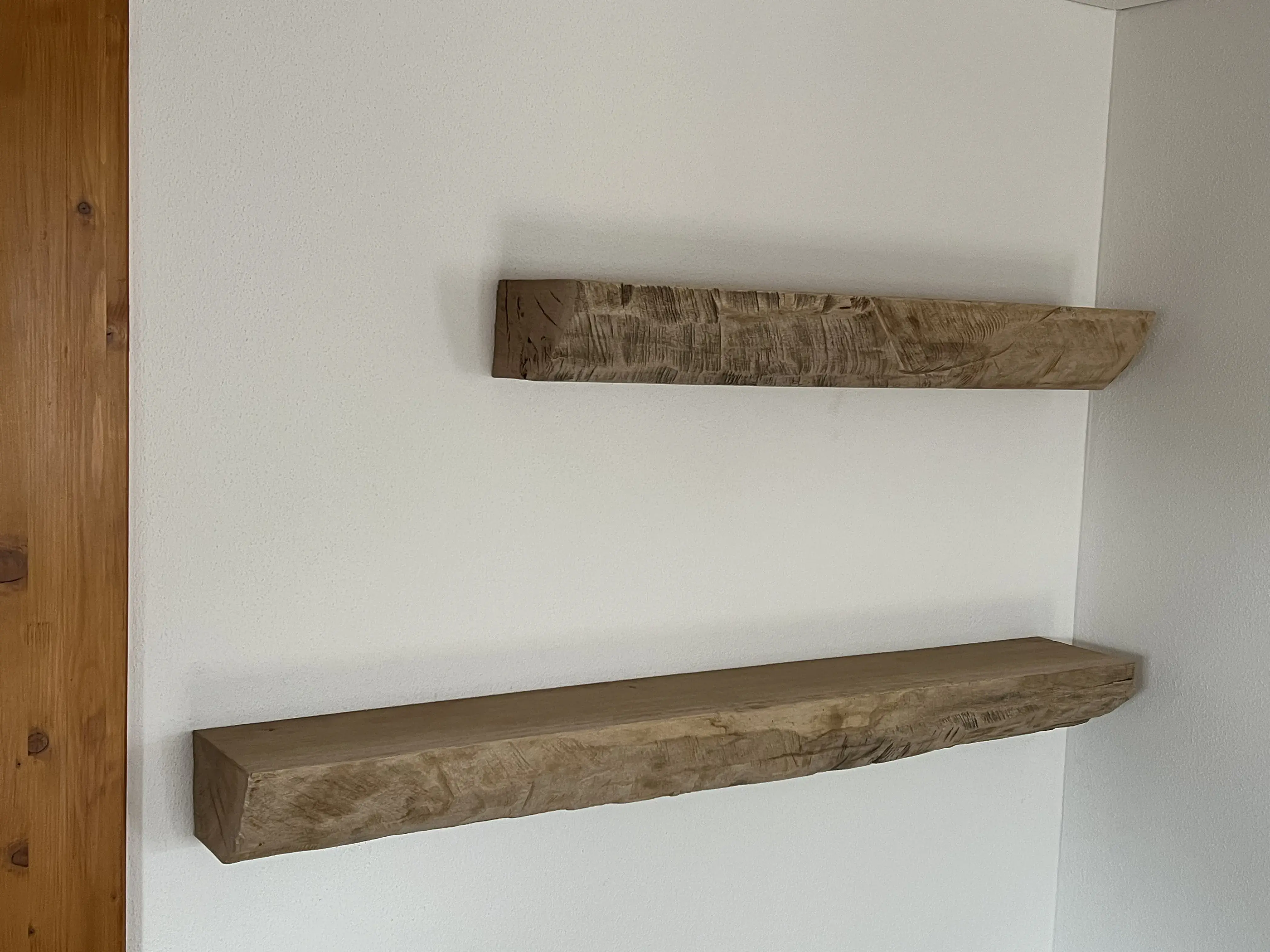 Zwei rustikale Holzbretter als schwebende Regale an einer weißen Wand.