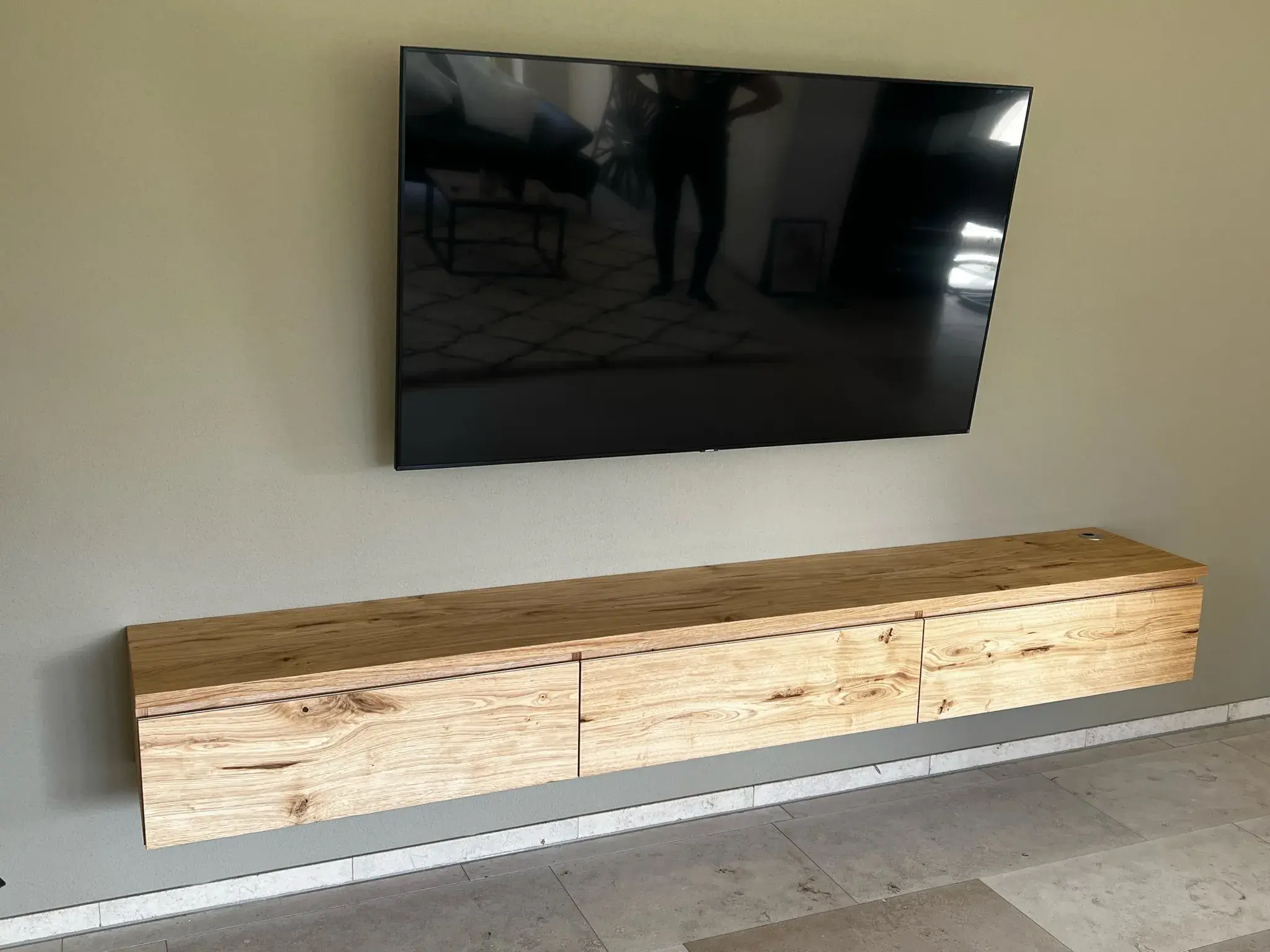 Flachbildfernseher an der Wand über einem schwebenden Holzsideboard