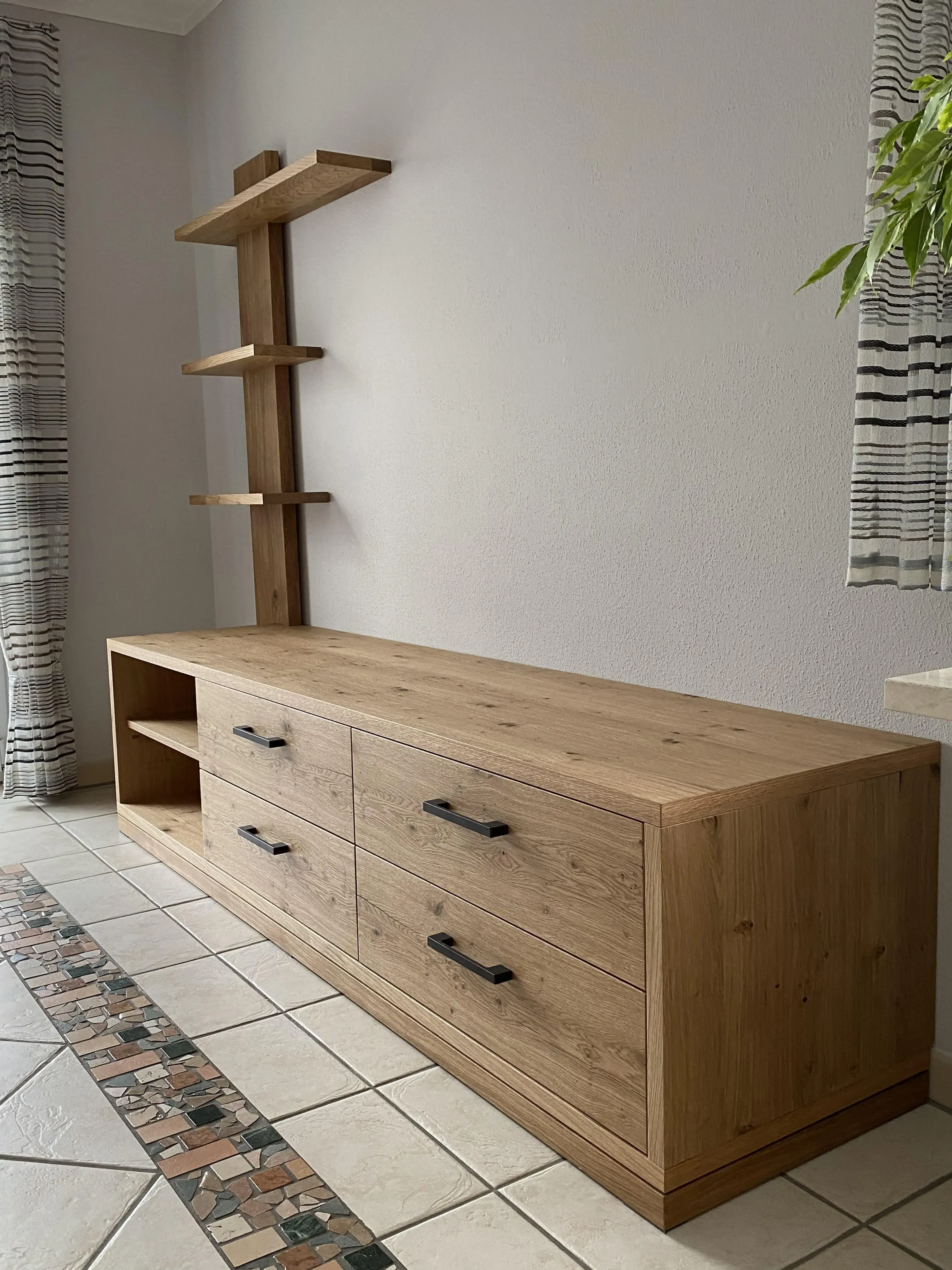 Holz-Kommode mit schwarzen Griffen und offenen Regalen an einer hellen Wand.