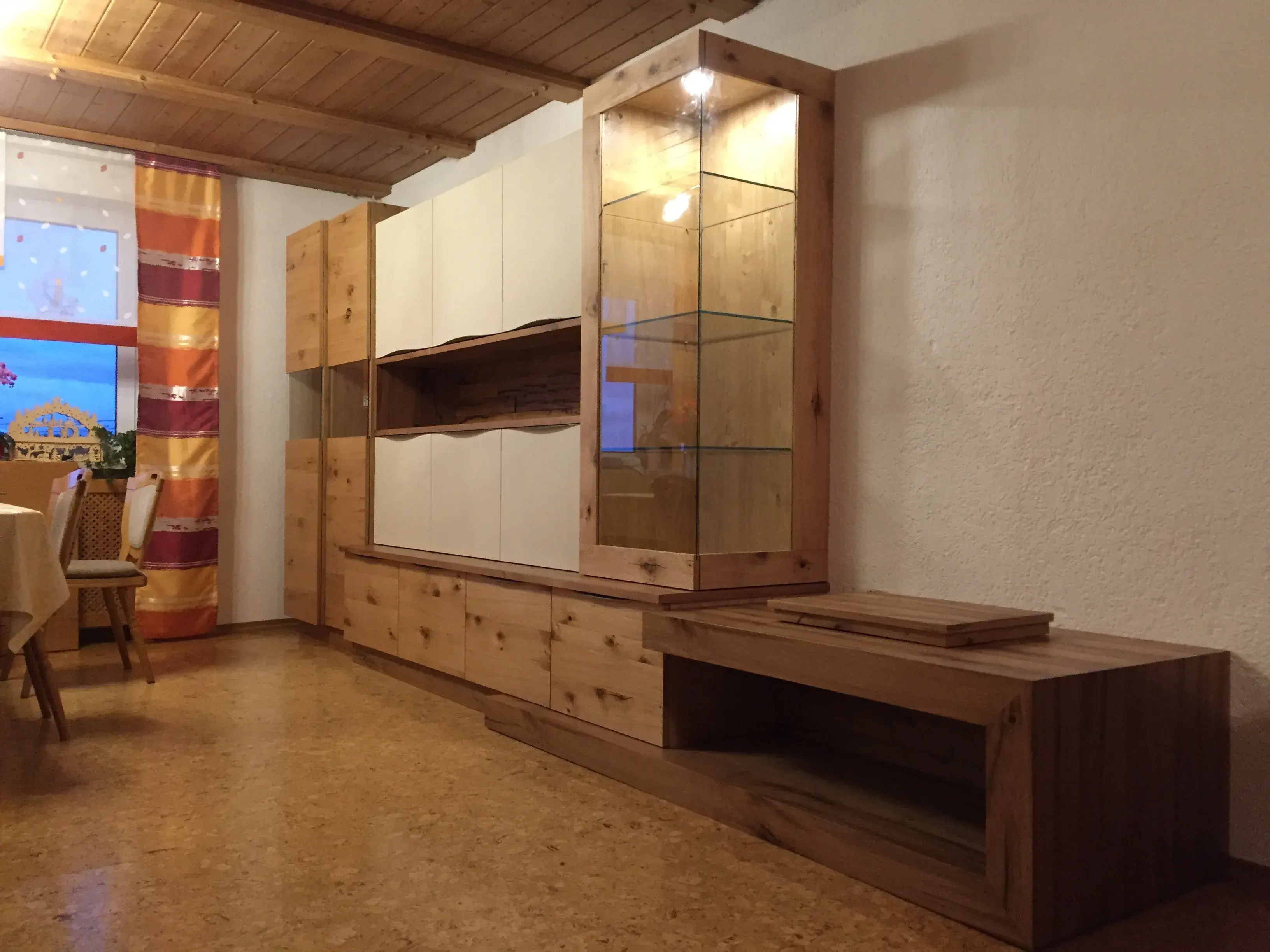 Holzwohnwand mit Glasvitrine in einem gemütlichen Wohnzimmer mit Holzboden und Decke.