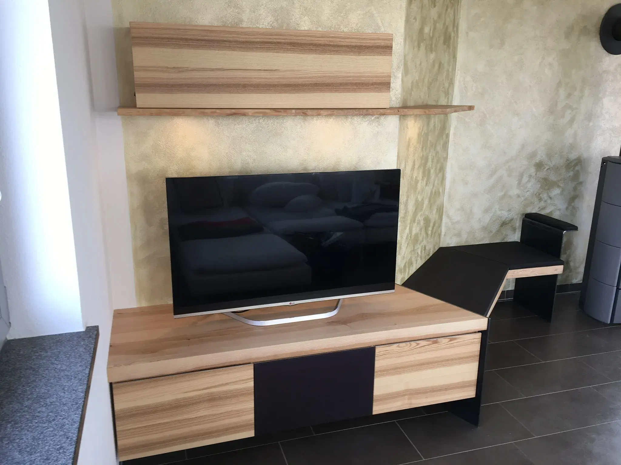 Flachbildfernseher auf Holz-TV-Möbel mit Regal vor hell gemusterter Wand.