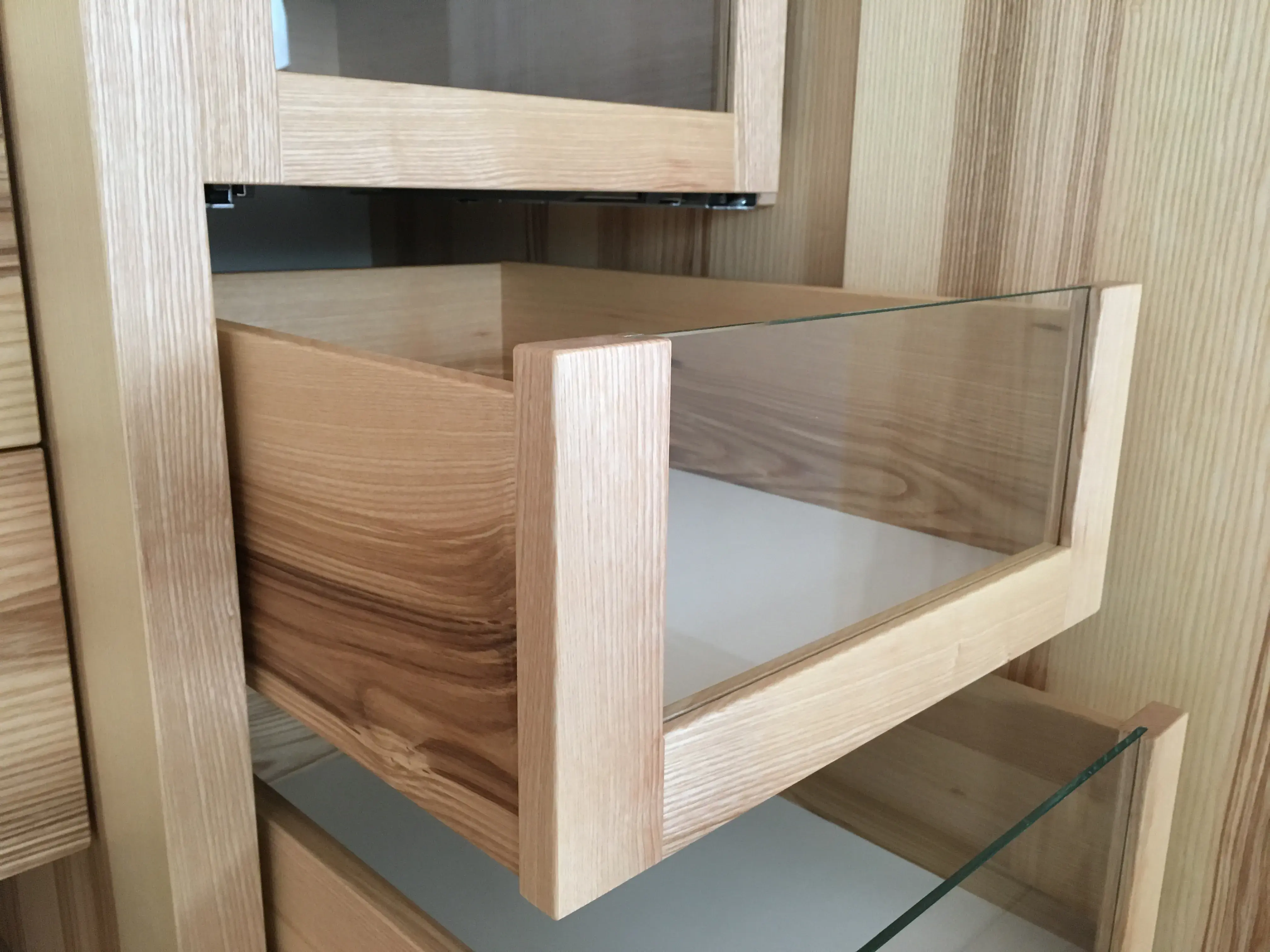Offene Holzschublade mit Glasfront in einem modernen Schrank.