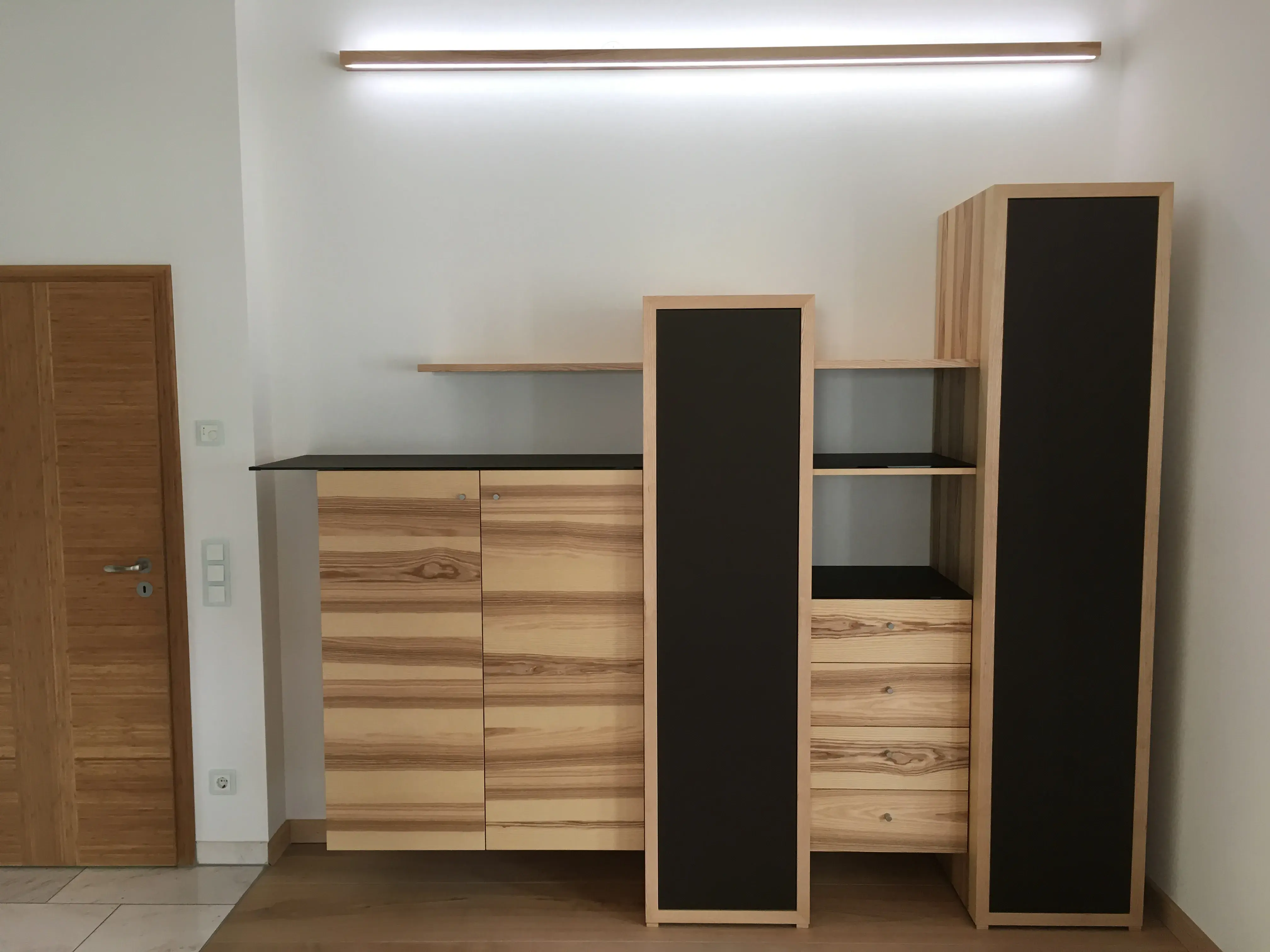 Modernes Sideboard aus Holz mit schwarzen Akzenten und indirekter Beleuchtung.